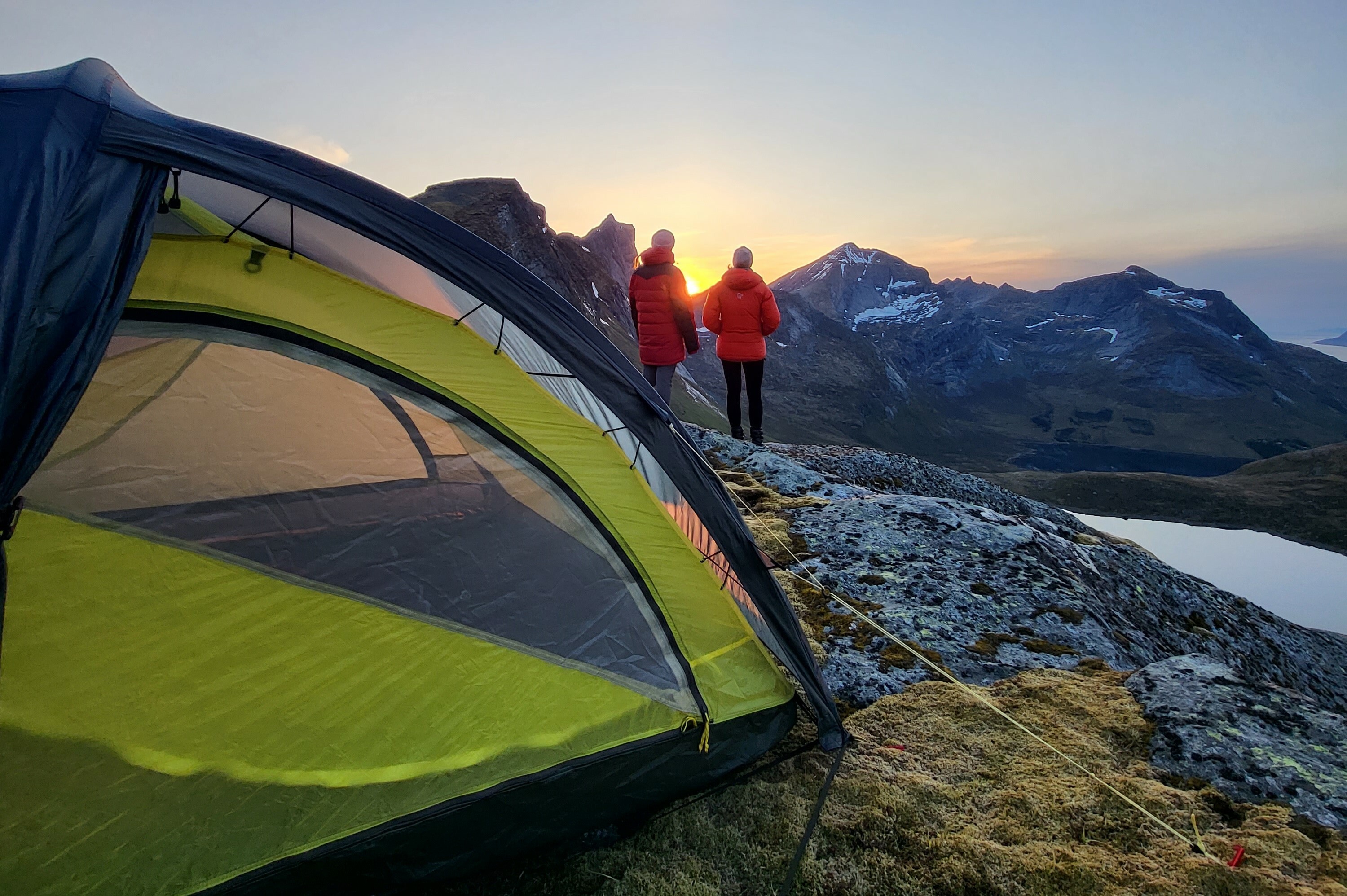 To turgåere nyter solnedgangen i fjellheimen. Teltet er satt opp i bakgrunnen.