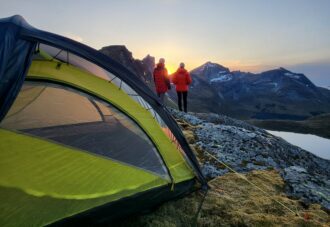 To turgåere nyter solnedgangen i fjellheimen. Teltet er satt opp i bakgrunnen.